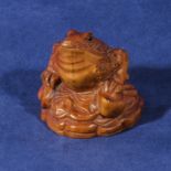 A carved wooden netsuke of a frog with a coin in it's mouth, signed
