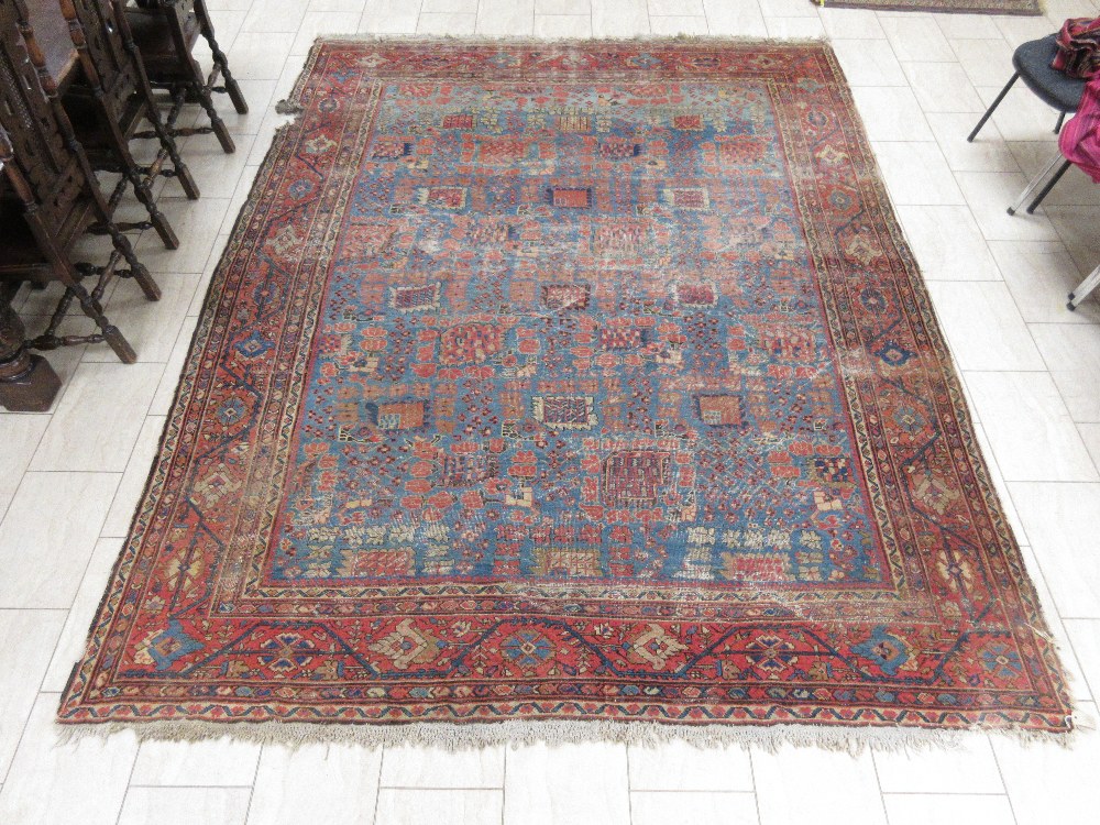 An old bordered Persian Carpet with red stylised motifs on a blue ground, principal border with