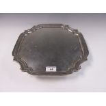 A George V silver square Salver with presentation inscription, shaped rim on four scroll feet,