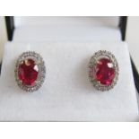 A pair of Ruby and Diamond Halo Earrings each claw-set oval-cut ruby within a frame of pavé-set