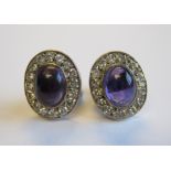 A pair of Amethyst and Diamond Cluster Earrings each rub-over set oval amethyst cabochon within