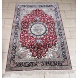 A bordered Persian silk Rug with central circular medallion surrounded by floral design on a red