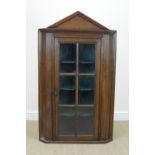 An antique oak hanging Corner Cupboard with single glazed door enclosing shaped shelves