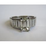 A Diamond Ring corner claw-set step-cut stone, 1.5cts, between trios of channel-set baguettes in