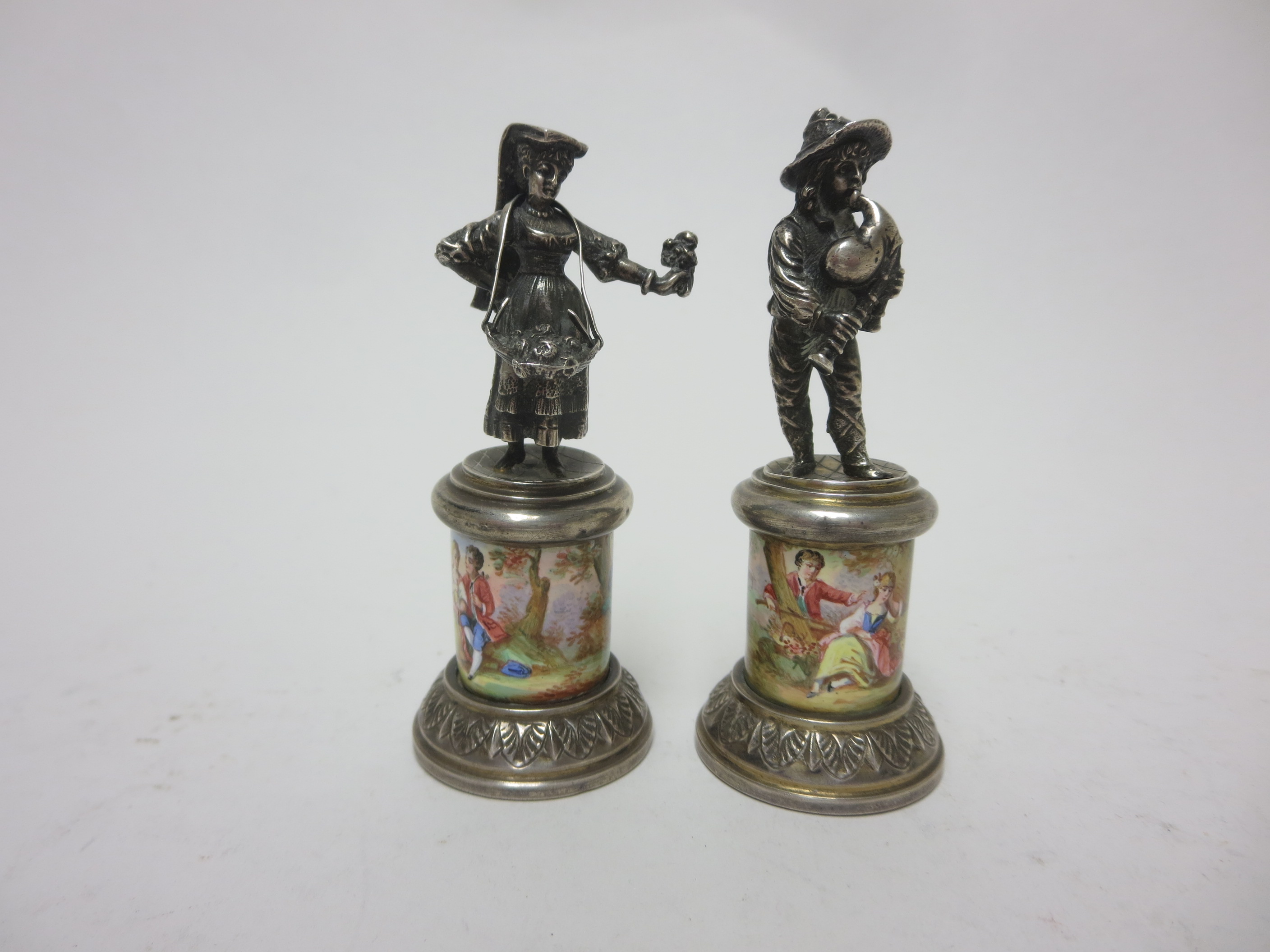 A pair of Continental silver Figures of flower girl and musician on circular pedestals enamelled