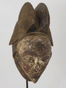 A Punu (West African) Mask, a feminine mask with elaborate coiffure, white kaolin face with full