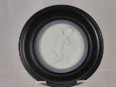 A Porcelain Plaque, depicting a cherub playing pipes, presented in an ebony frame.