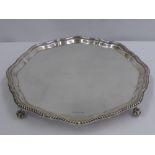 A Solid Silver Salver, the salver having a scalloped and ribboned edge, on scroll laurel feet,