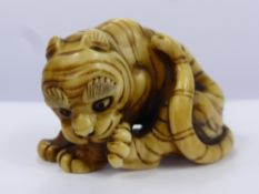 A Meiji Period Japanese Ivory Netsuke, depicting a crouching tiger licking his paw, character