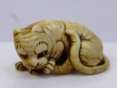 A Meiji Period Japanese Ivory Netsuke, depicting a crouching tiger licking his paw, character