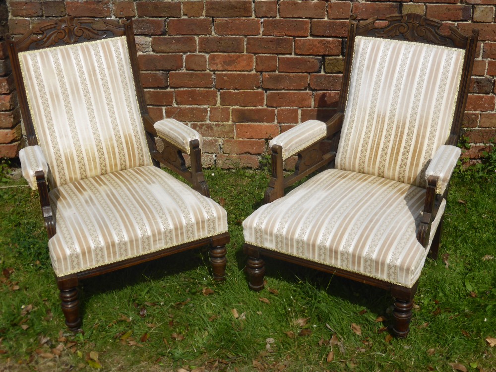 A Pair of Edwardian Arm Chairs, with swept arms, on turned legs and casters, decorative carving to