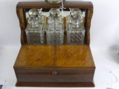 An Edwardian Oak Mirrored Back Tantalus, with three cut glass decanters, having carrying handles