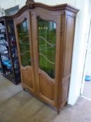 An Oak Armoire Style Display Cabinet, with green glazed fronted doors and shell motif to top, four