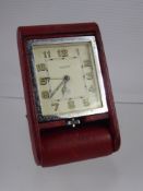 A Jaeger Le Coultre 8 Day Travelling Alarm Clock, in a folding red leather case.