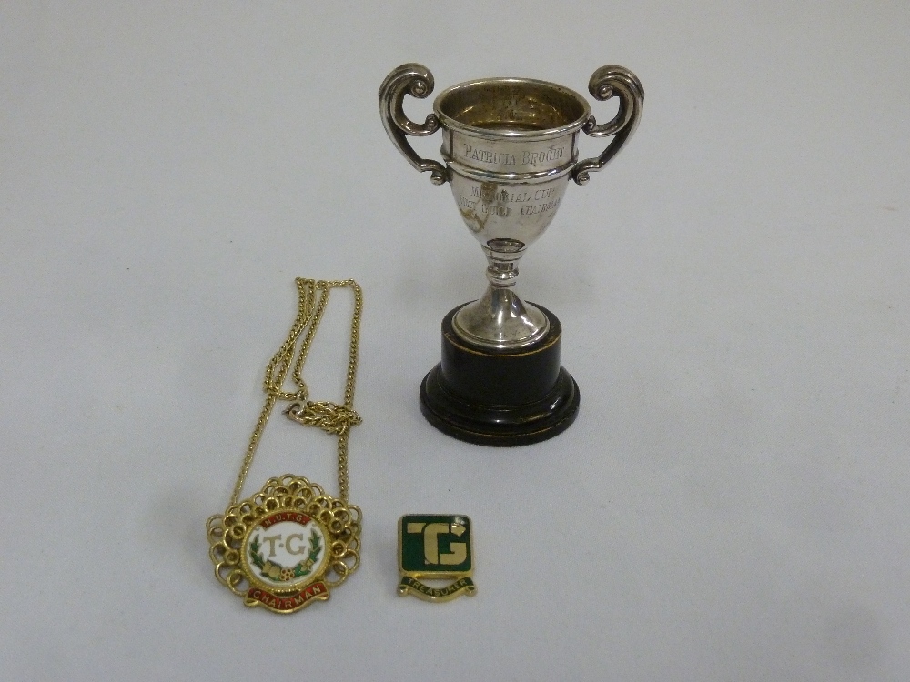 A miniature silver trophy cup, a gilt metal and enamel badge and another metal and enamel badge