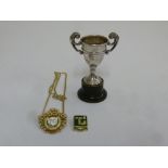 A miniature silver trophy cup, a gilt metal and enamel badge and another metal and enamel badge