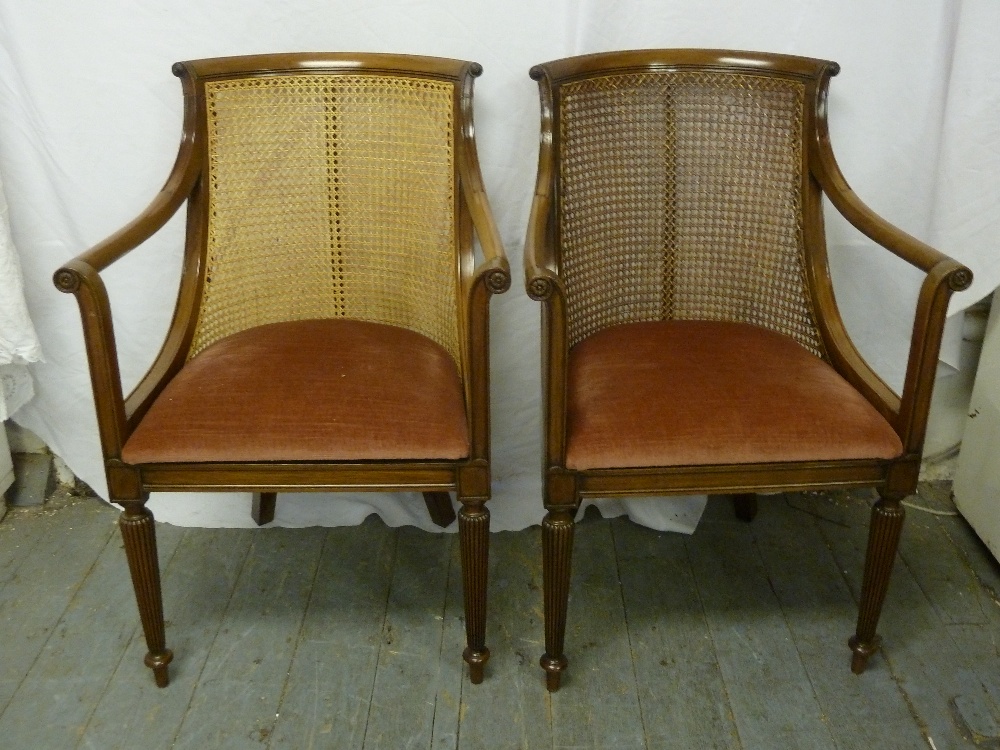 A pair of early 20th century mahogany and bergere armchairs with upholstered seats on fluted