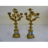 A pair of gilded metal and porcelain two light candelabra, leaf chased branches on cylindrical base