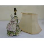 A porcelain table lamp in the form of a lady in 18th century costume and with pink silk shade