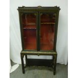 A Chinese style lacquered cabinet, with glazed doors and painted side panels on rectangular stand