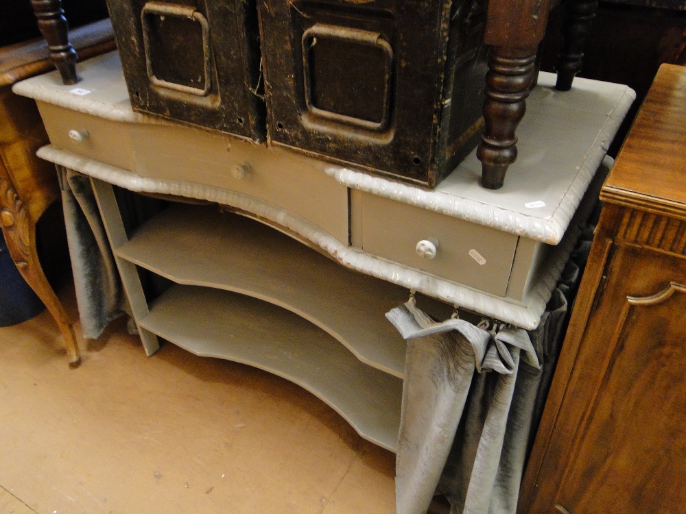 A painted serpentine front dressing table with fitted drawers and open shelves.