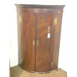 A late George III bow-fronted mahogany corner cupboard, wall-hanging, enclosed by a pair of doors