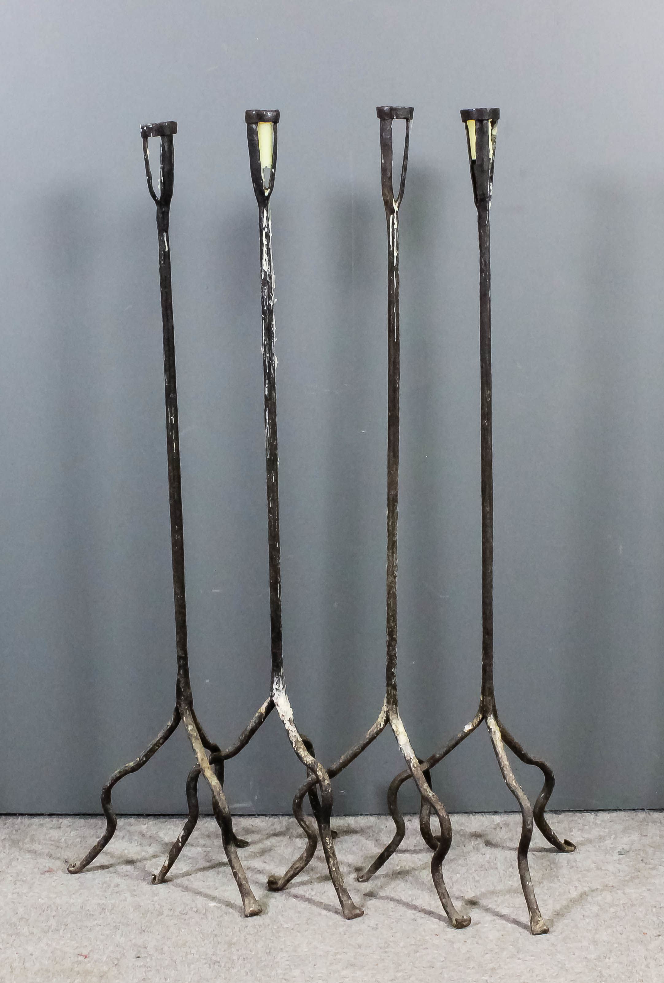 A set of four wrought iron floor standing candle holders, the plain rod stems supported on three