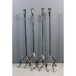 A set of four wrought iron floor standing candle holders, the plain rod stems supported on three