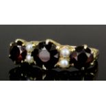 A late Victorian gold coloured metal mounted three stone garnet and seed pearl ring, the central