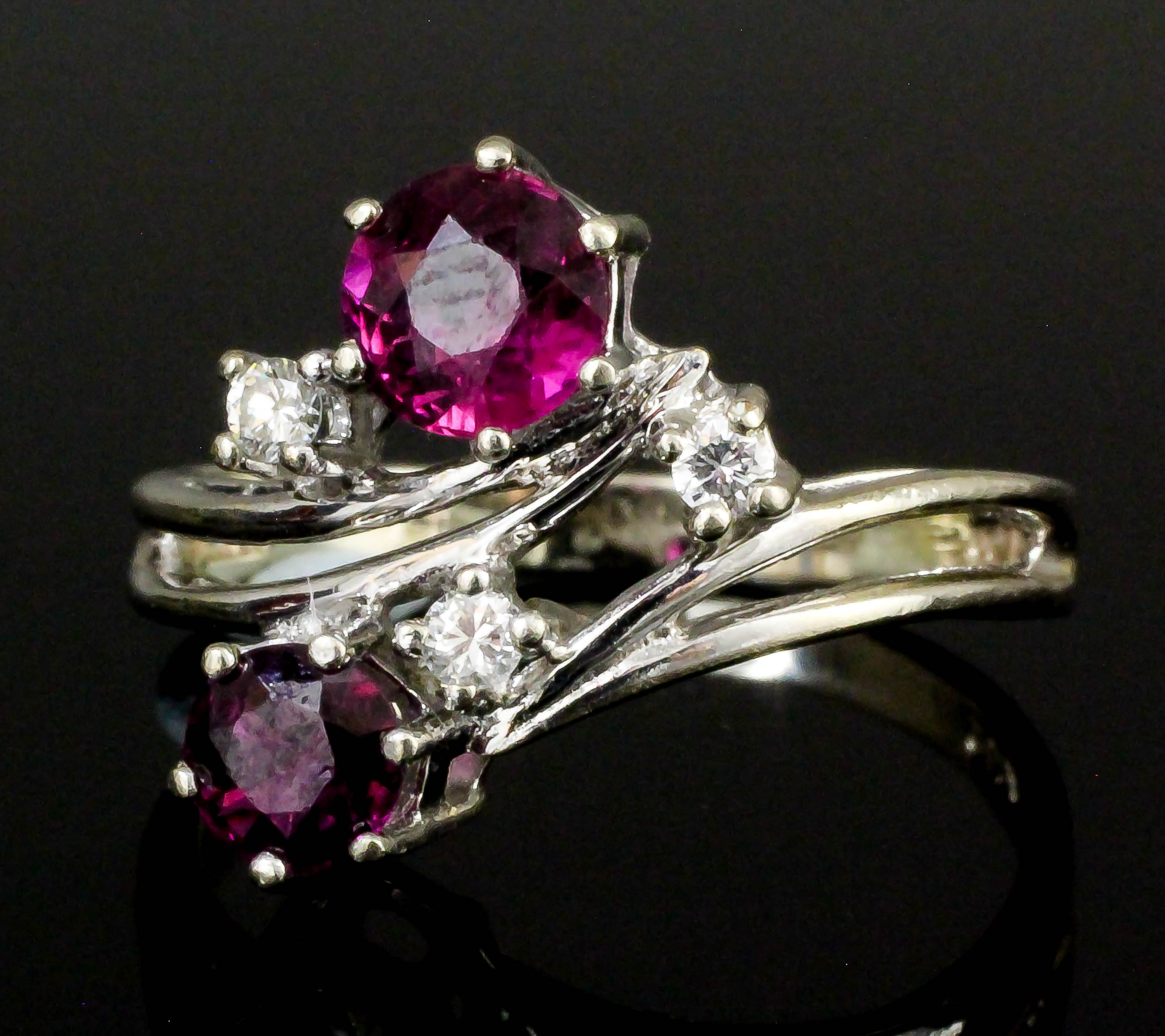 A modern 14ct white gold ruby and diamond crossover pattern ring, the two circular cut rubies .