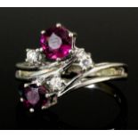 A modern 14ct white gold ruby and diamond crossover pattern ring, the two circular cut rubies .