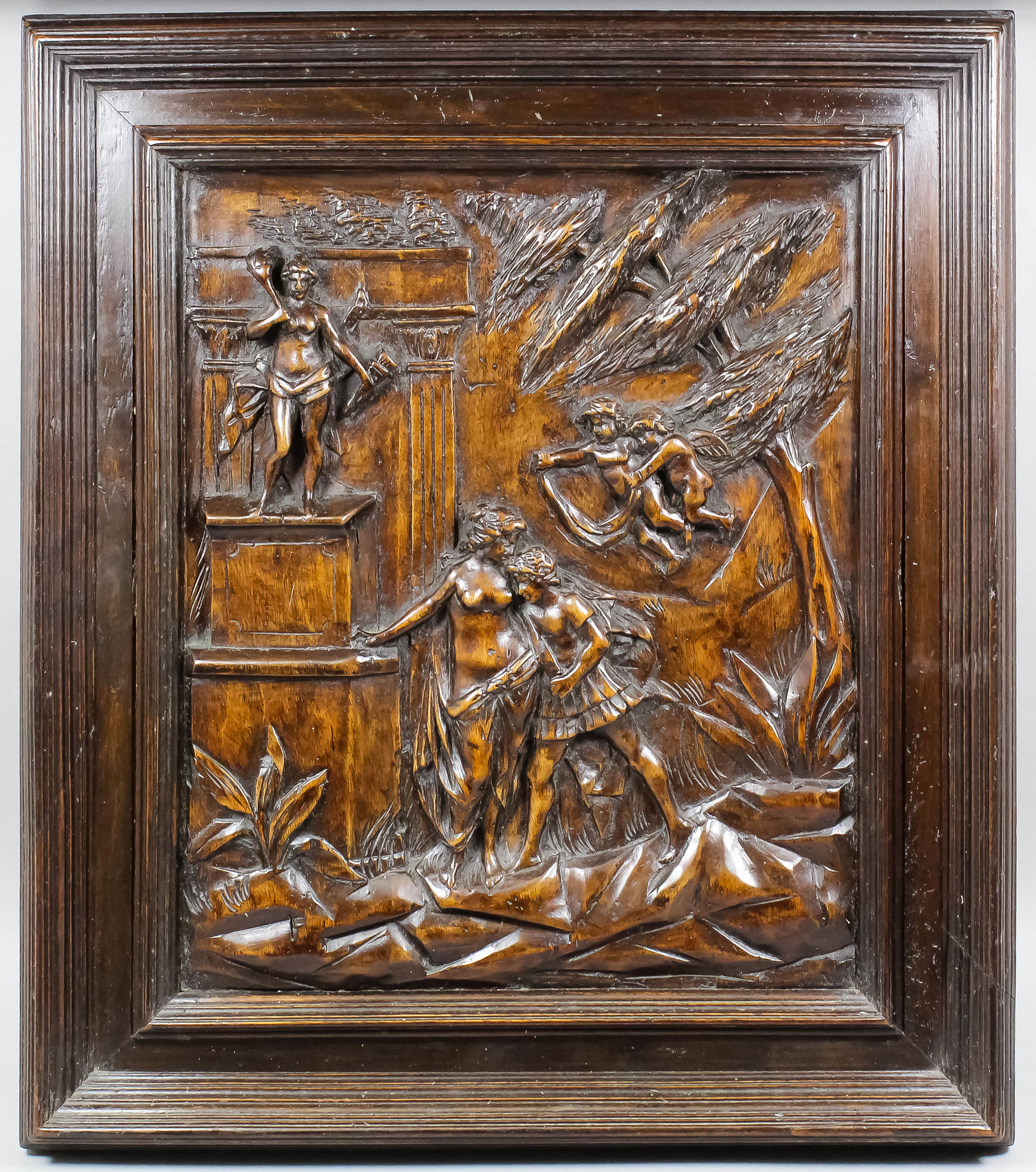 A 16th Century carved walnut panel with a classical scene of male and female figures beside a statue