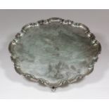 A George V silver circular salver of Georgian design with moulded piecrust rim, on four scroll feet,