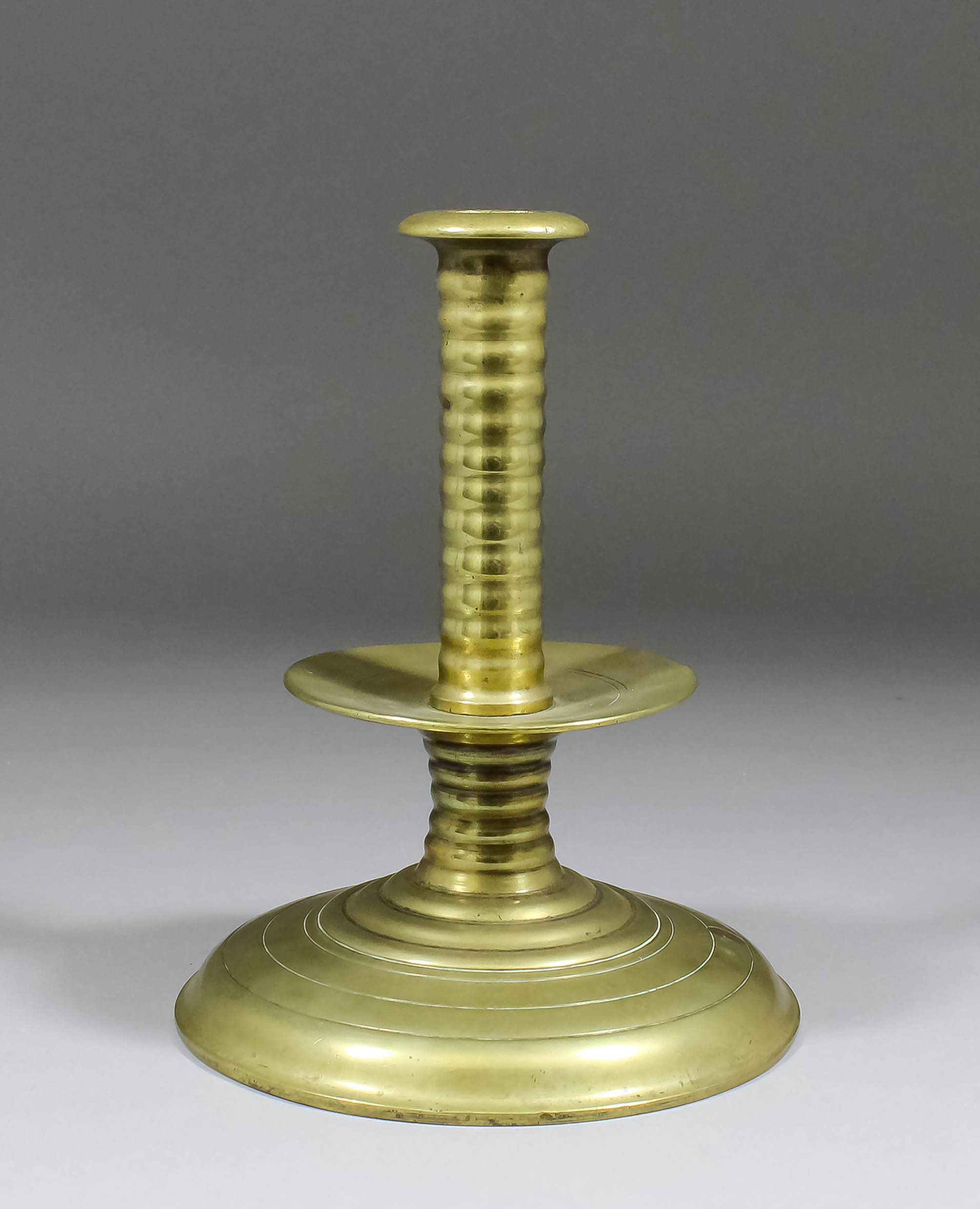 A brass candlestick, the rib shaft with central drip tray above a shallow trumpet base, English, 7.
