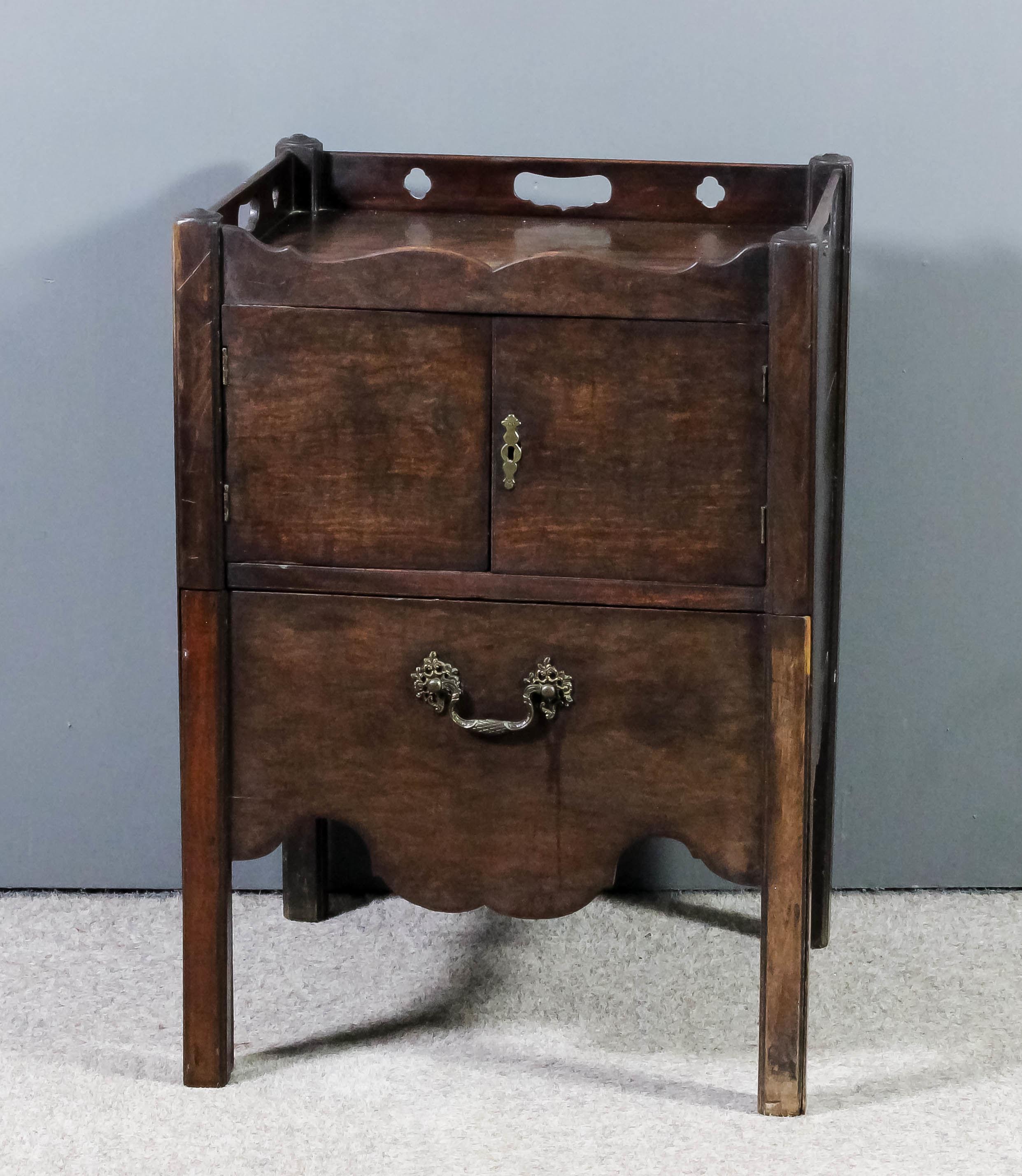 A George III mahogany tray top bedside cabinet, the shaped top with three handle cut-outs enclosed