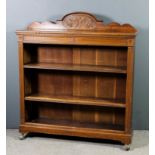A Victorian oak open front bookcase with shaped upstand, carved with scroll and ribbon ornament,