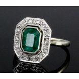 A 1920s silvery coloured metal mounted emerald and diamond ring, the oblong emerald cut stone