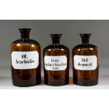 Three chemists amber tinted glass jars and stoppers, each with black and white label worded "Ol