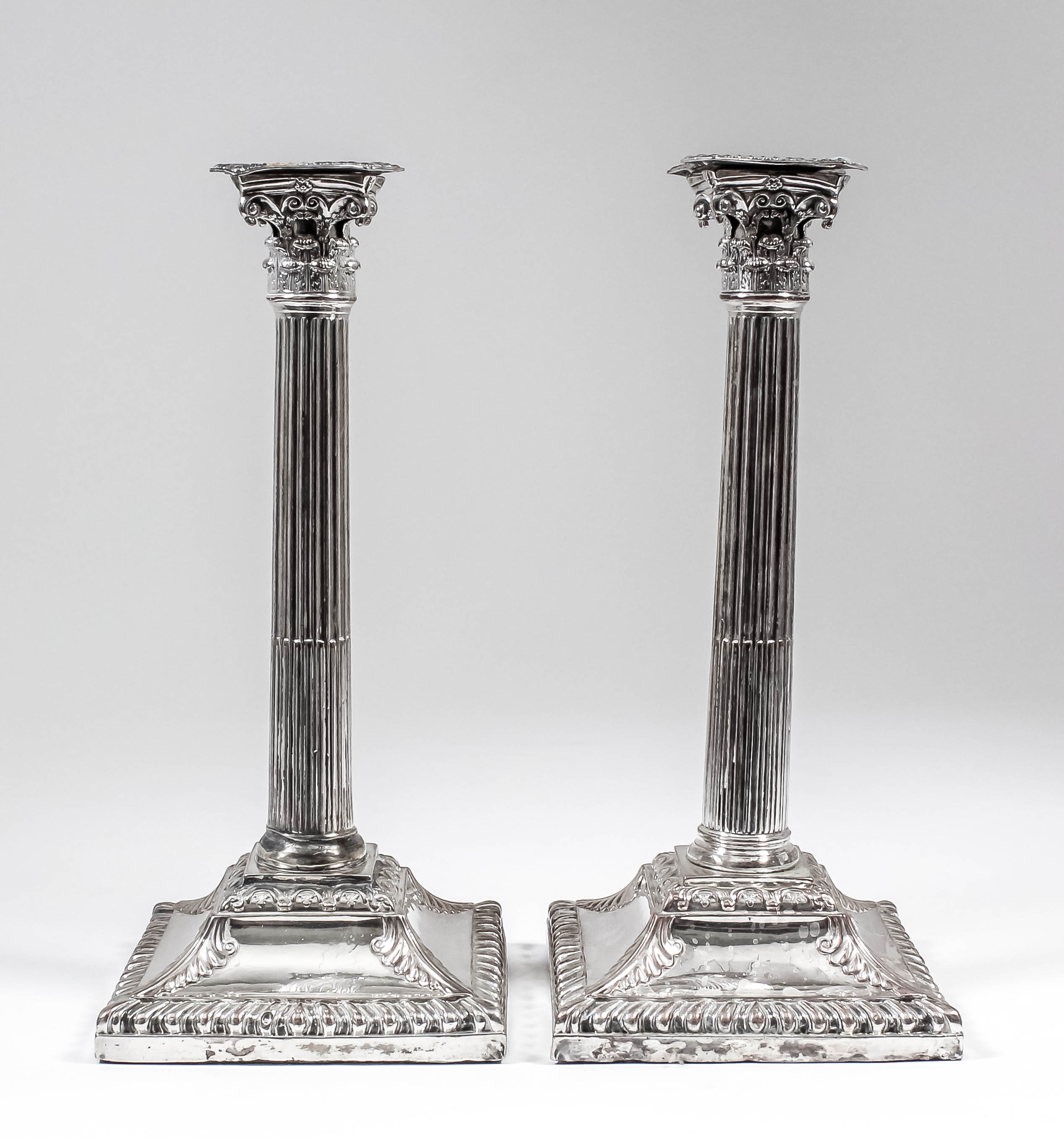 A pair of plated pillar candlesticks with cast Corinthian capitals and stop fluted columns, the