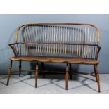 An ash and elm seated stick back Windsor settee, with two-tier back, on turned legs and stretcher,