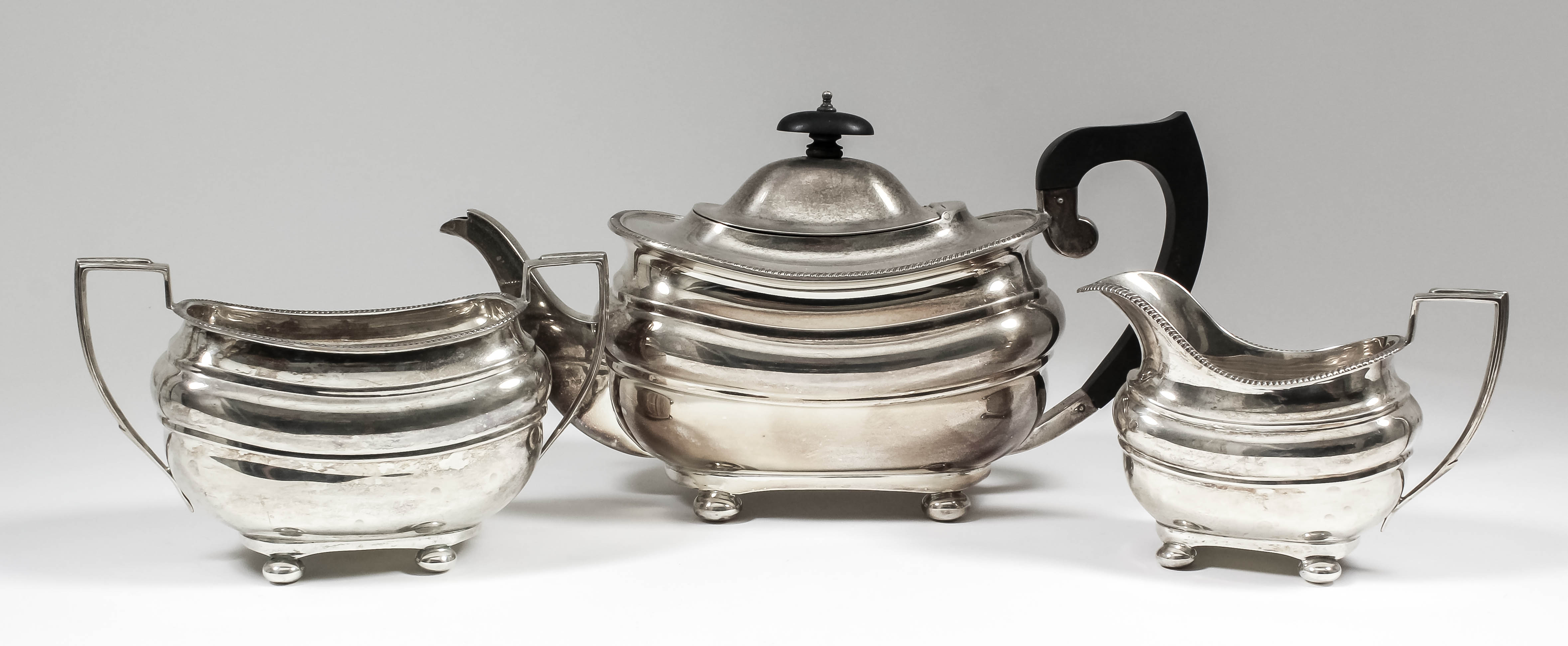 A George V silver rectangular three piece tea service with gadroon mounts, bulbous bodies, angular