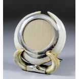 A silvery metal mounted boars tusk circular photograph frame with easel stand, to take photograph