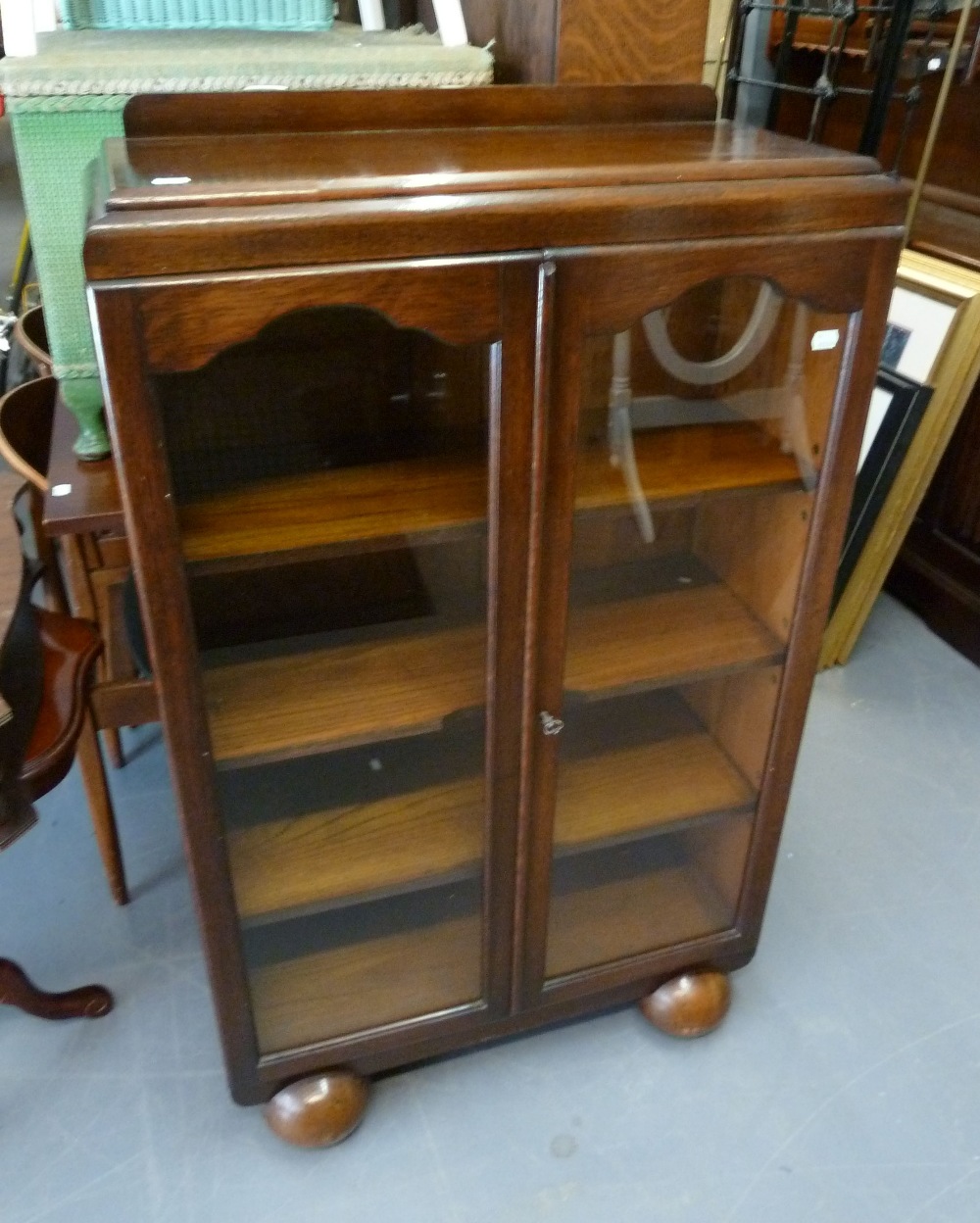 AN OAK DWARF BOOKCASE, WITH THREE ADJUSTABLE SHELVES ENCLOSED BY TWO GLAZED DOORS, ON TWO BALL FEET,