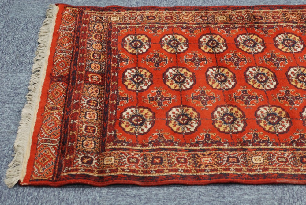 MACHINE MADE 'BOKHARA' RUG, with three rows of guls on a crimson field, 6'3" x 4'5" and an EASTERN