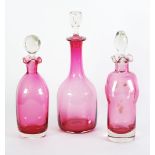 THREE CRANBERRY GLASS DECANTERS, with clear glass stoppers, 9 3/4" - 11 1/2" (24.8cm - 29.2cm)