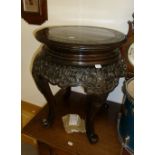 AN ORIENTAL CARVED WOOD LOW CIRCULAR URN STAND WITH ORNATE APRON, ON FOUR LEGS