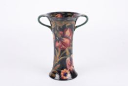 A William Moorcroft tubelined trumpet vasewith twin handles, decorated with red flowers and