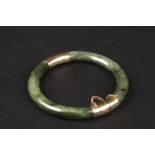 A Chinese dark green hardstone and yellow coloured metal bangle
with safety chain, Condition: