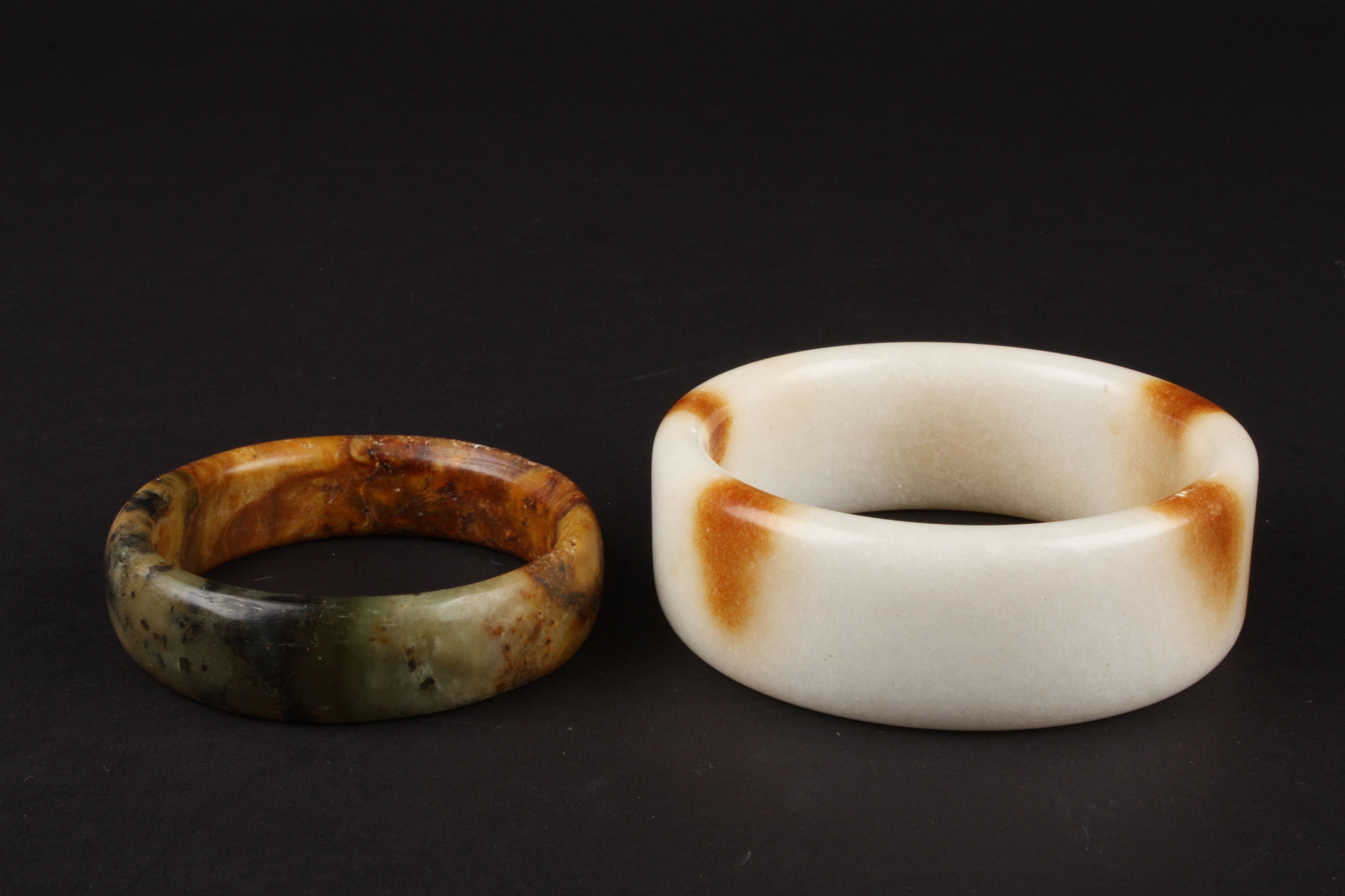 A large 20th Century Chinese white and brown polished stone bangle and another spinach and ochre