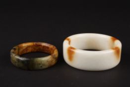 A large 20th Century Chinese white and brown polished stone bangle and another spinach and ochre